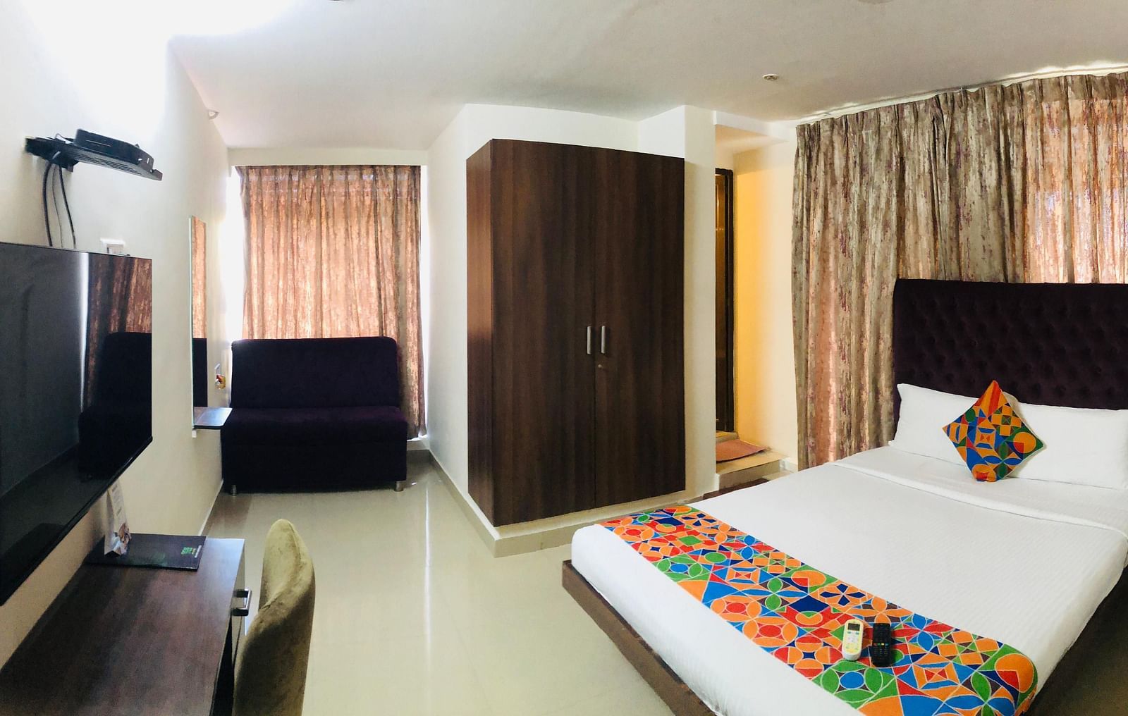 View of Premium Room in Astra Hotels and Suites, HSR Sector 1 where a bed, TV, desk, chair and wardrobe are arranged in a spacious room.
