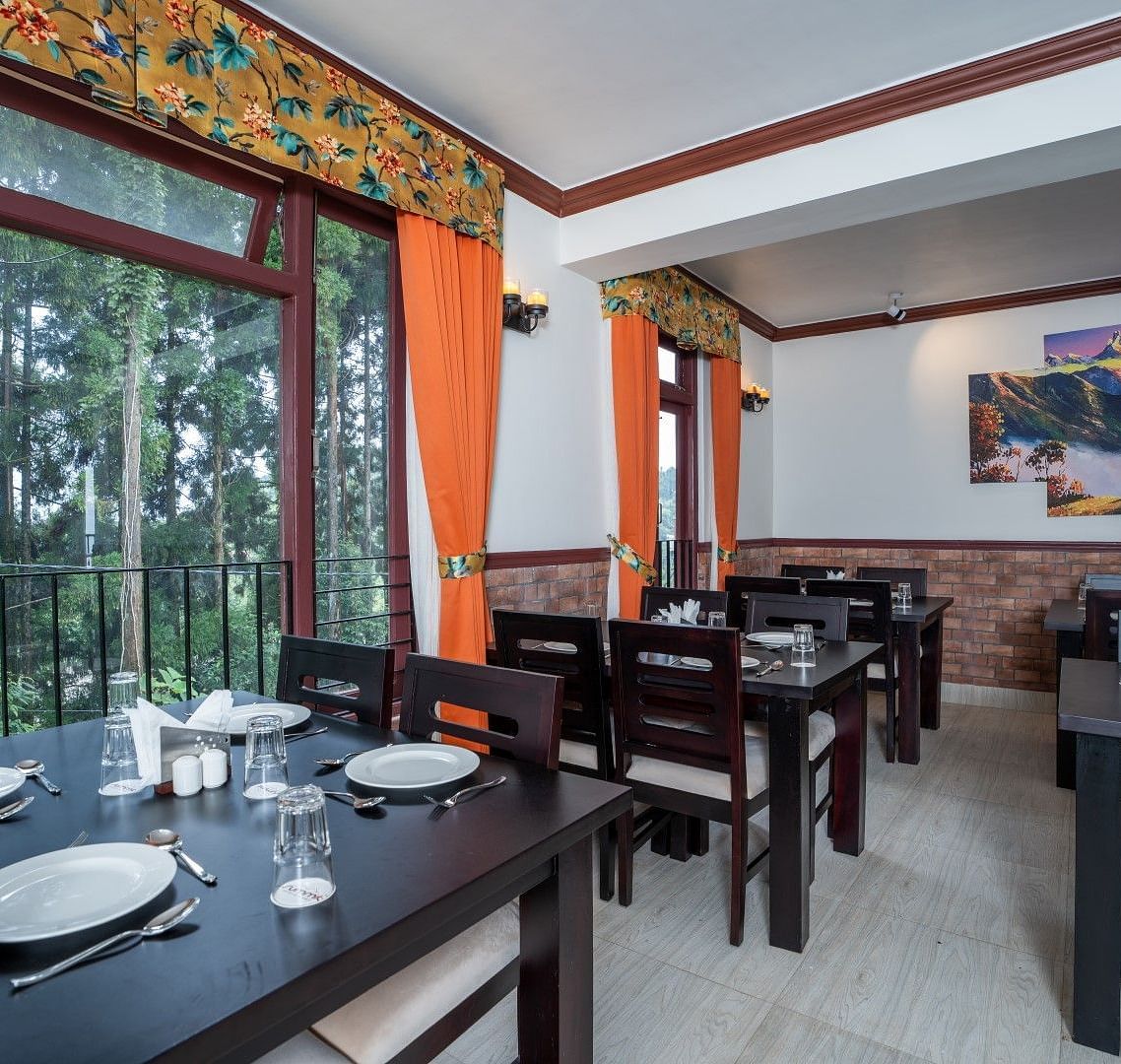 Image of a dining space with large windows and seating area at Summit Sherpa Mountain Hotel & Spa, Kalimpong