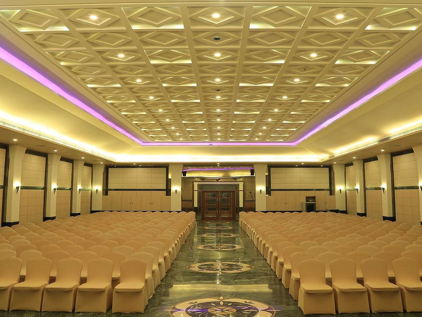 Over view of DS Mahal Hall at Dhanalakshmi Srinivasan Hotels, Perambalur with  chairs arranged in theatre seating and chandelier on top. 