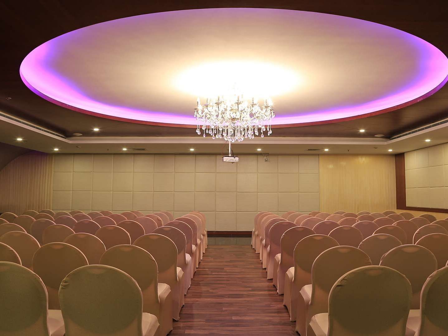 Orchid Hall at Dhanalakshmi Srinivasan Hotels, Perambalur with  chairs arranged in theatre seating and chandelier on top. 