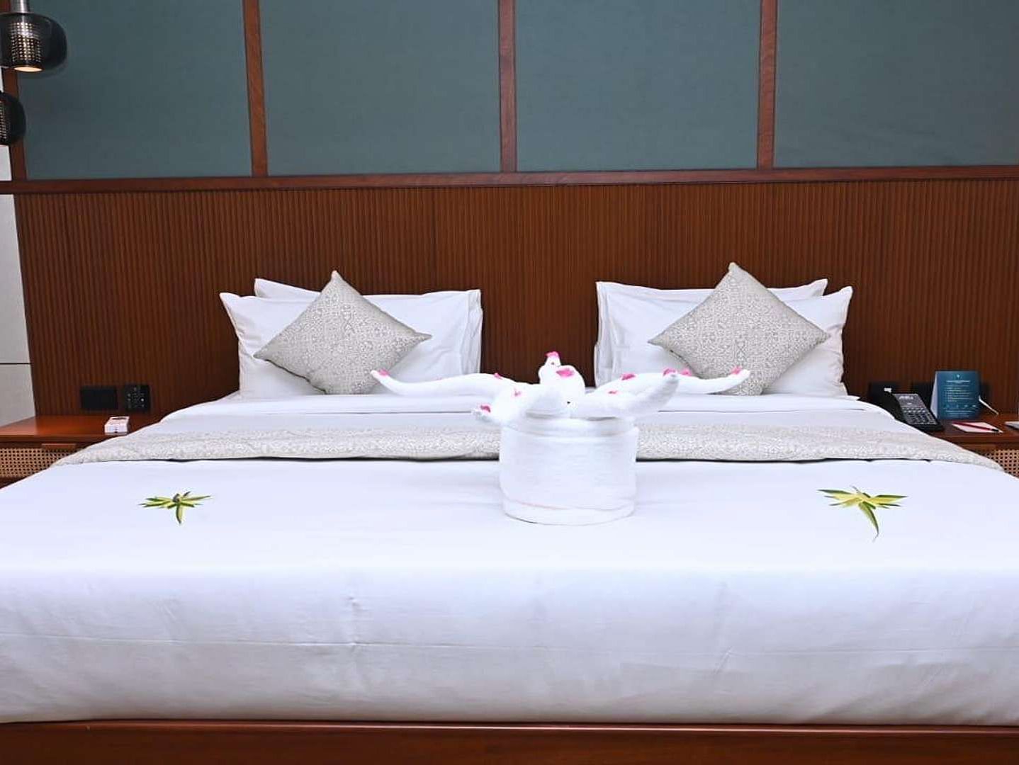 Close up of a Executive Suite at Dhanalakshmi Srinivasan Hotels, Perambalur featuring a bed with white linens, and dark wood headboard