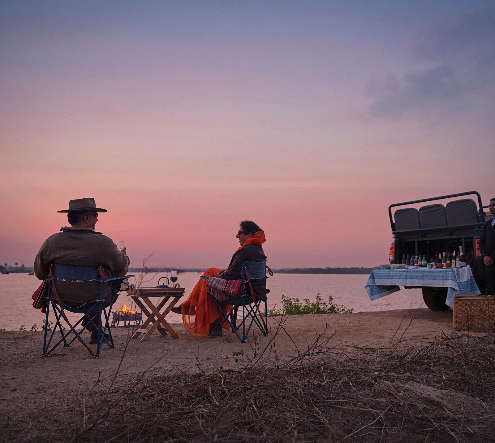 couple soaking in the pink hues of the sunset with a picturesque lake in front of them at dev shree , deogarh