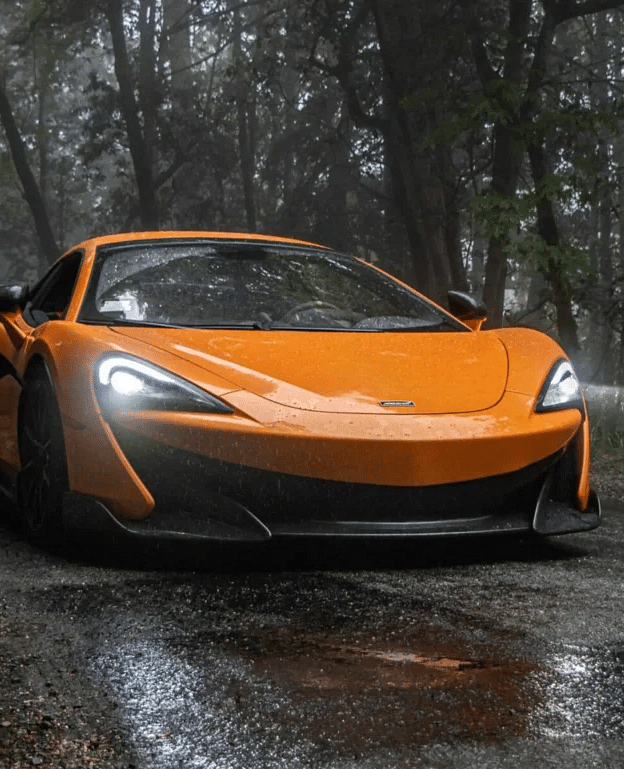 an orange colored sports car driving through a wet muddy trail
