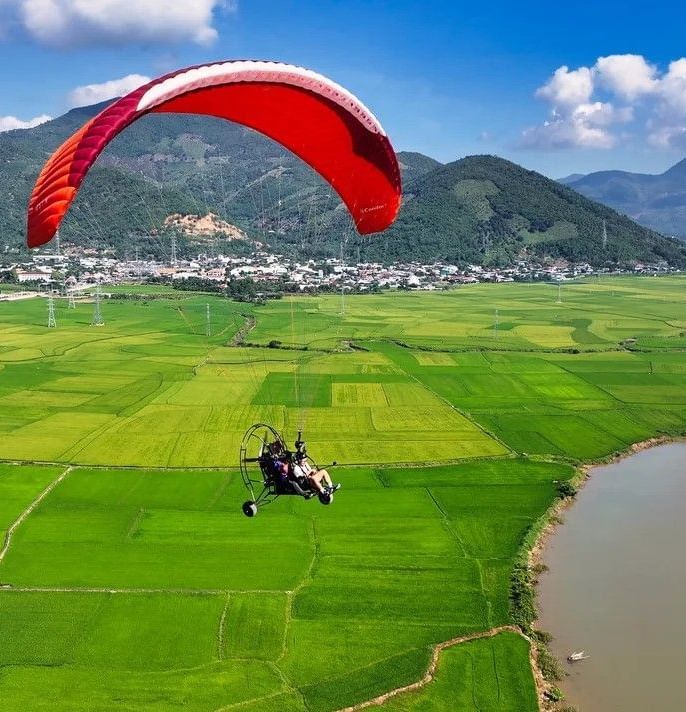 Paragliding above lush green rice fields and a tranquil lake, offering breathtaking countryside views near Alibu Resort.