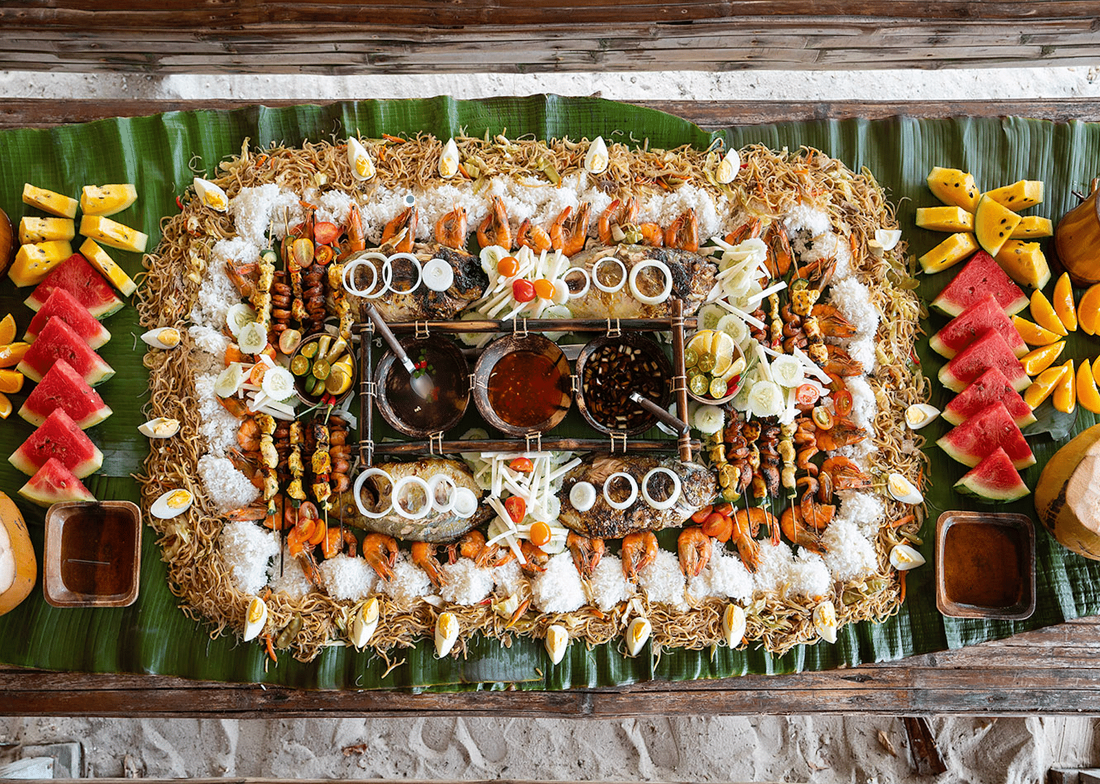 Table with assorted seafood, fruits, and rice dishes arranged on leaves at Flower Island Resort.