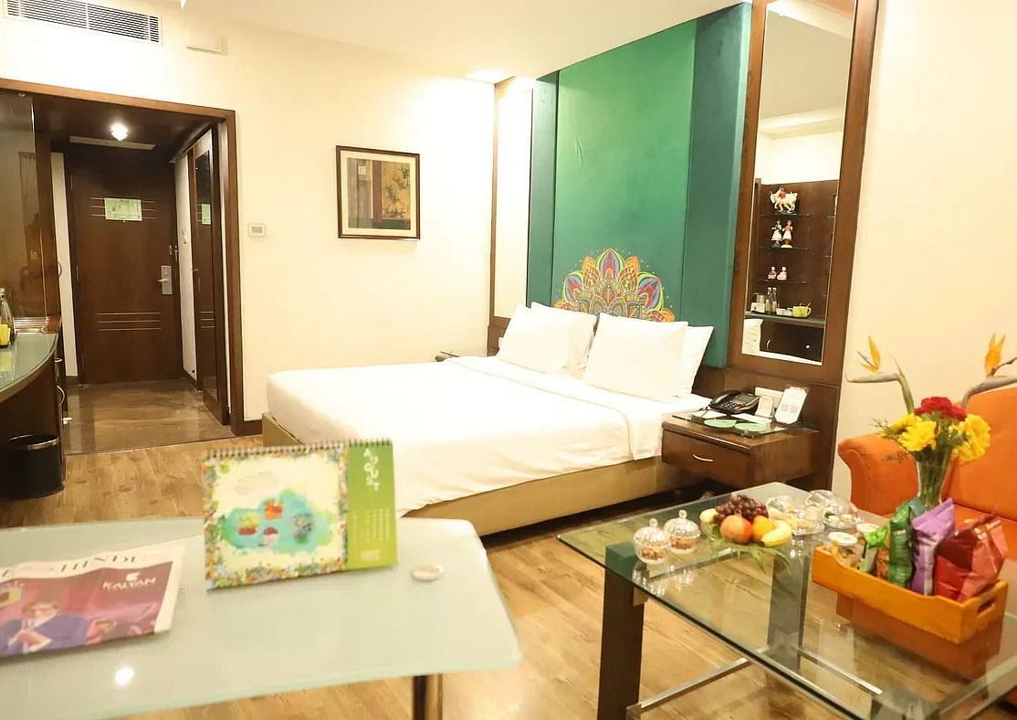 A well-appointed hotel room with a large bed, an orange armchair, a glass table, and modern decor | Superior Room | Regency Madurai by GRT Hotels