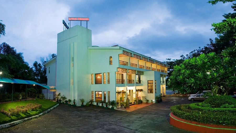 facade image of VITS Kamats Resort Silvassa  with dense green trees on the side and dark sky in the background - VITS Hotels & Resorts