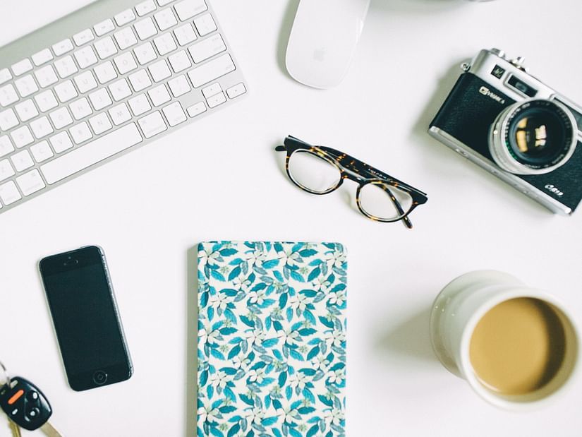 Flat lay composition of various office and personal items, including tech gadgets, stationery, and a beverage.