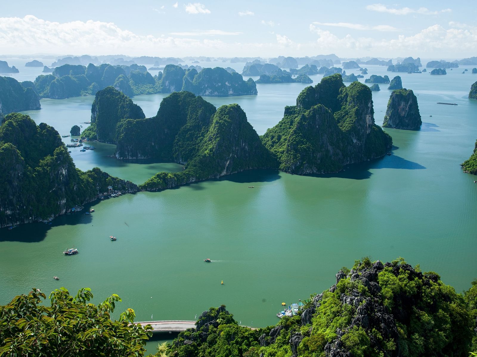 An aerial view of Ha Long Bay with hills covered by greenery scattered around a waterbody. 