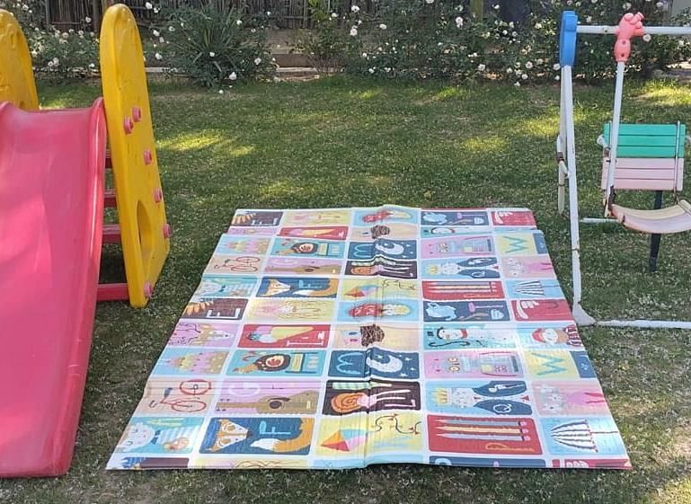An outdoor play area featuring a small slide, a swing set, and a colourful play mat spread on the grass.