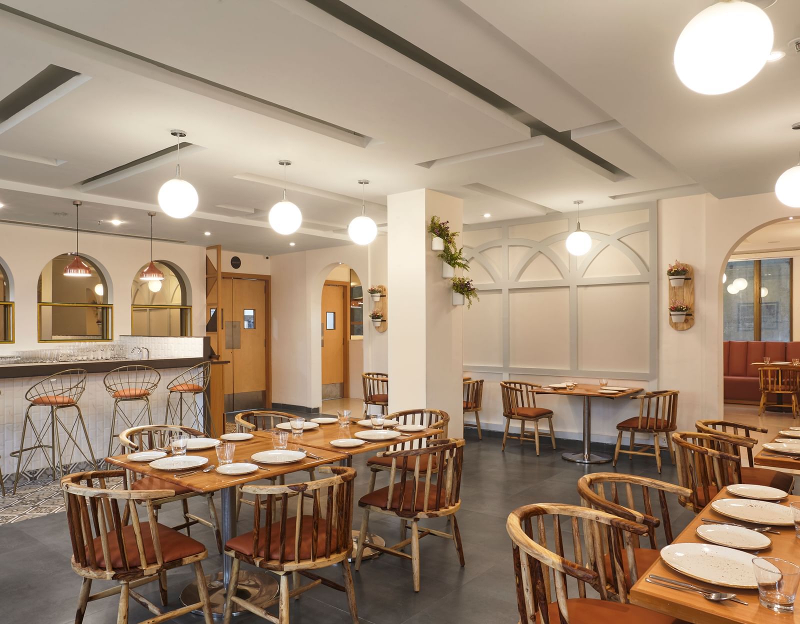 The spacious dining hall at Monday Hotels Mahape, Navi Mumbai, with multiple wooden tables and a central bar.