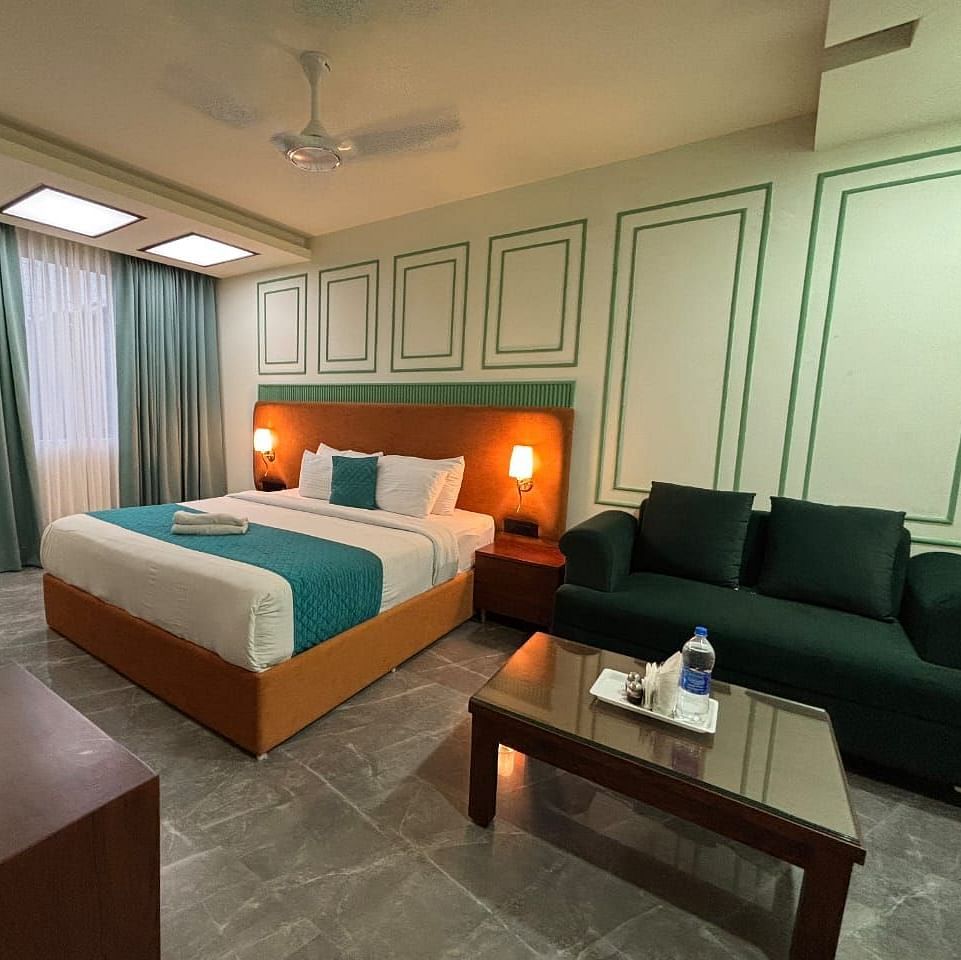 A spacious room with a double bed, a dark green sofa, and a wooden coffee table - Asian Suites IFFCO Metro, Gurgaon