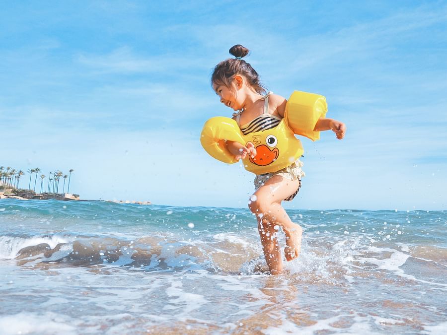 Child playing in shallow waves with inflatable float at the beach near Heritage Village Resorts & Spa, Goa.