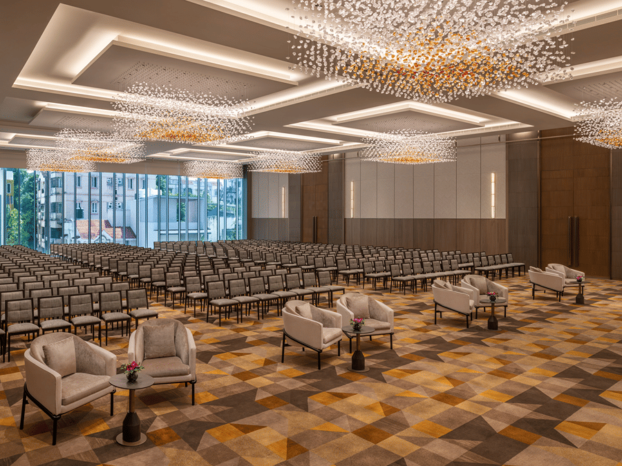 The grand banquet hall of Ballroom 1 arranged in theatre seating with plush armchairs in the front row and crystal chandeliers above at The Residency Towers Chennai.