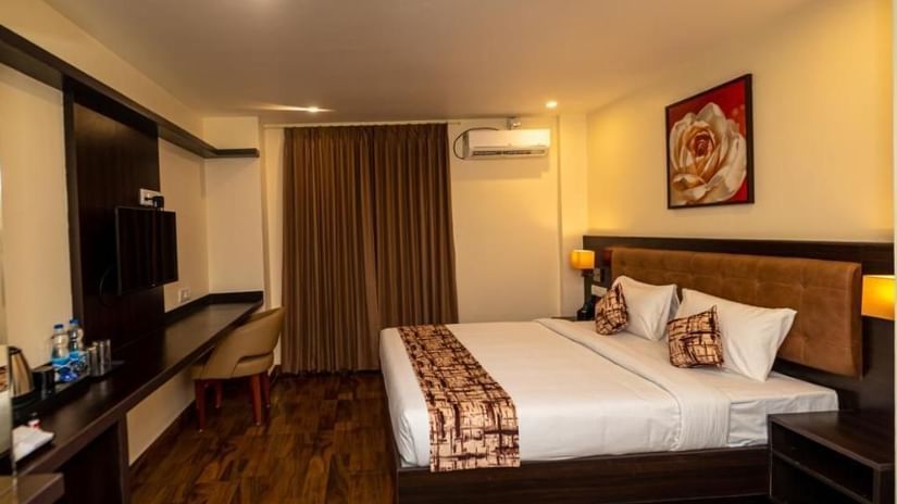 Wide view of a spacious Super Deluxe Room at VITS Select, Bengaluru, furnished with a king size bed, air-conditioning, a wall-mounted TV, and wooden flooring.