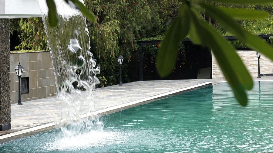 Swimming pool with water cascading from a feature wall, leaves in the foreground.