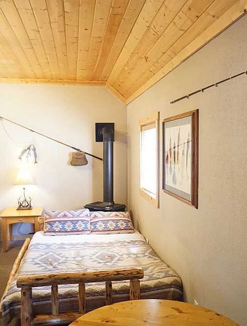 A well-lit room at Shaver Lake Village Hotel with a double bed and wooden paneling along the ceiling.