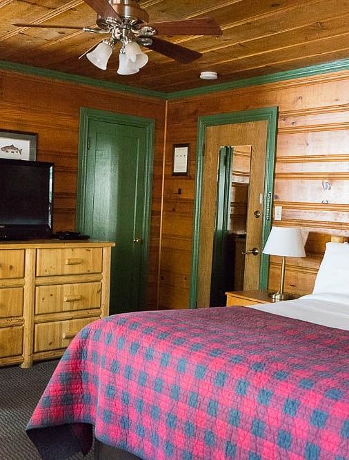 A wood-paneled room at Shaver Lake Village Hotel with a double bed, a brown cabinet, and wooden paneling throughout.