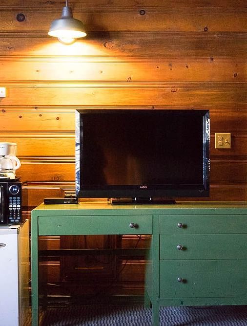 A wooden table with a TV placed on it, lit by a spotlight at Shaver Lake Village Hotel.