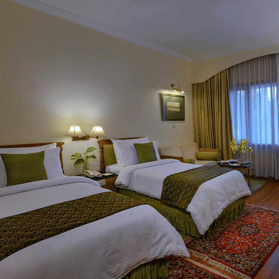 A Standard Room at The Clarks Varanasi featuring twin beds with matching rugs, full-length curtains and a flat-screen television.