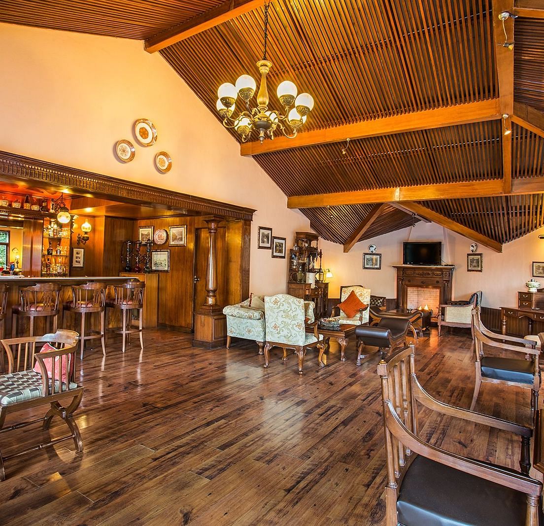 An image of indoor view of the bar at The Naini Retreat, Nainital, with sets of chairs and tables placed around the chandelier on the ceiling.