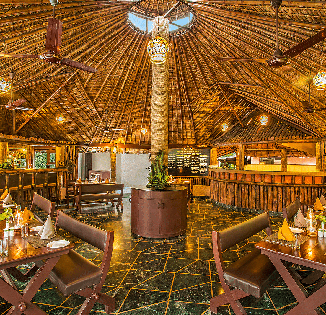 An image of a bar with wooden interiors, wooden chairs and tables, with plants filled at every corner - The Riverview Retreat, Corbett