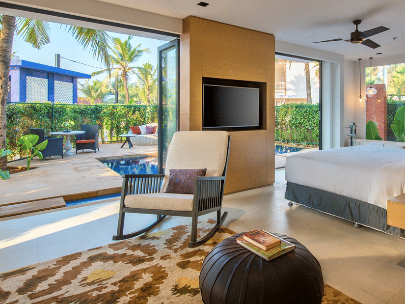 Luxurious poolside room with large glass doors, tropical garden views, cosy seating area, and a spacious bed for a relaxing stay at Azaya Beach Resort Goa
