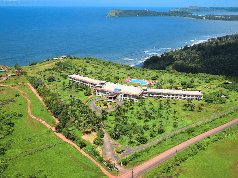 Aerial view of Kohinoor Samudra Beach Resort, Ratnagiri, overlooking the Arabian Sea, with lush green landscapes, landscaped gardens, and an outdoor swimming pool.