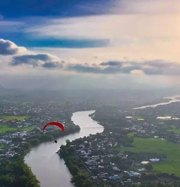Paragliding over lush green landscapes and winding rivers at sunset, an exciting aerial sport experience near Alibu Resort.