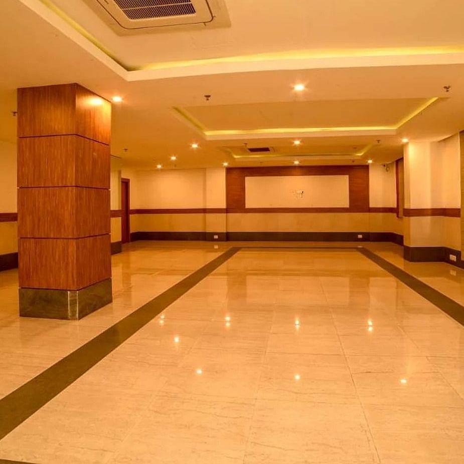 An image of a spacious banquet hall with installed lights in the ceiling - An image of a reception lobby featuring a reception desk , and a seating area for the guest - Max Hotel Jabalpur