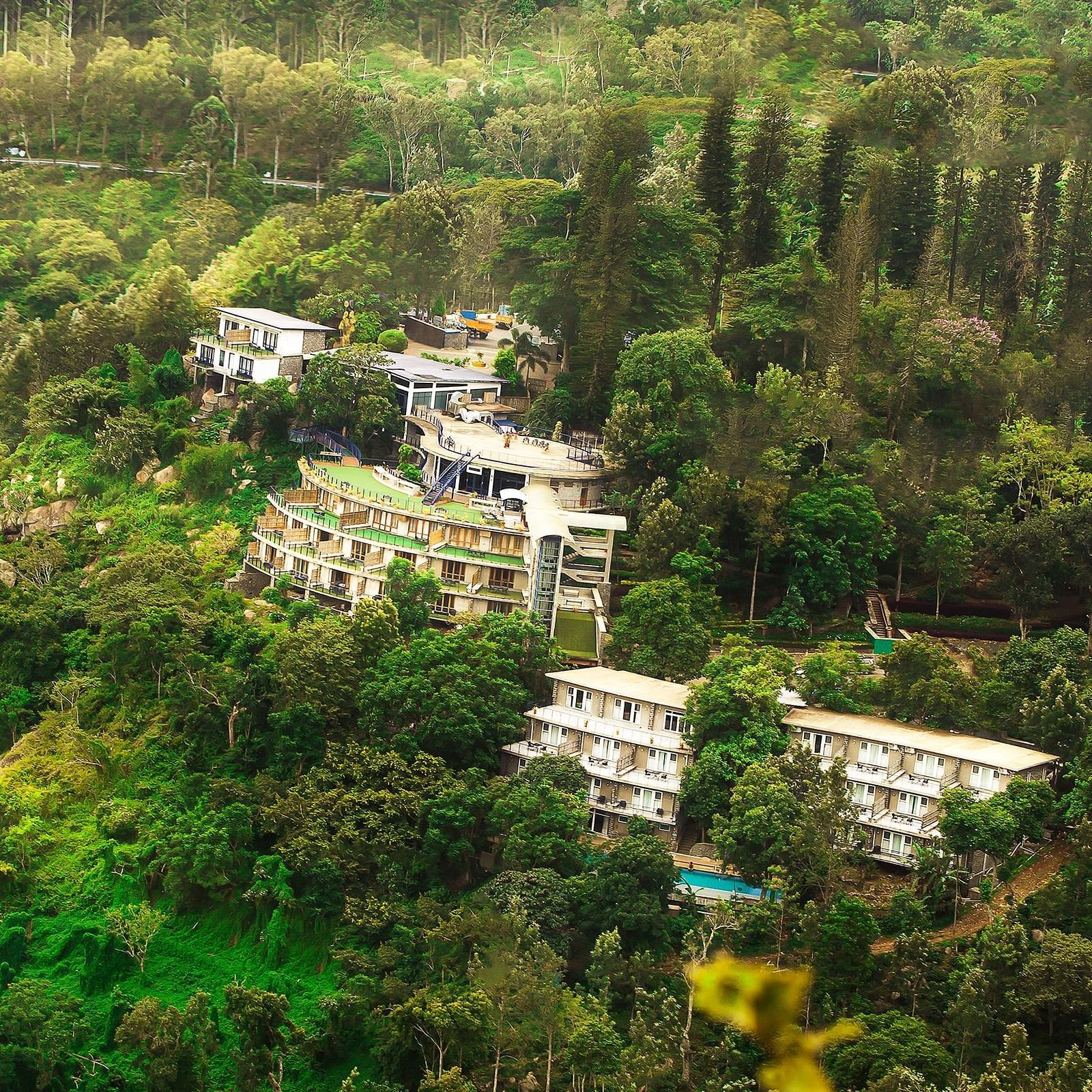 Drone shot of the hotel surrounded by mountains with sun light hitting the lush greenery - Great Trails Yercaud by GRT Hotels