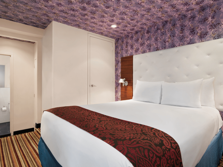 Modern bedroom at Night Hotel Broadway with a neatly made bed, patterned ceiling design, and soft, welcoming lighting.