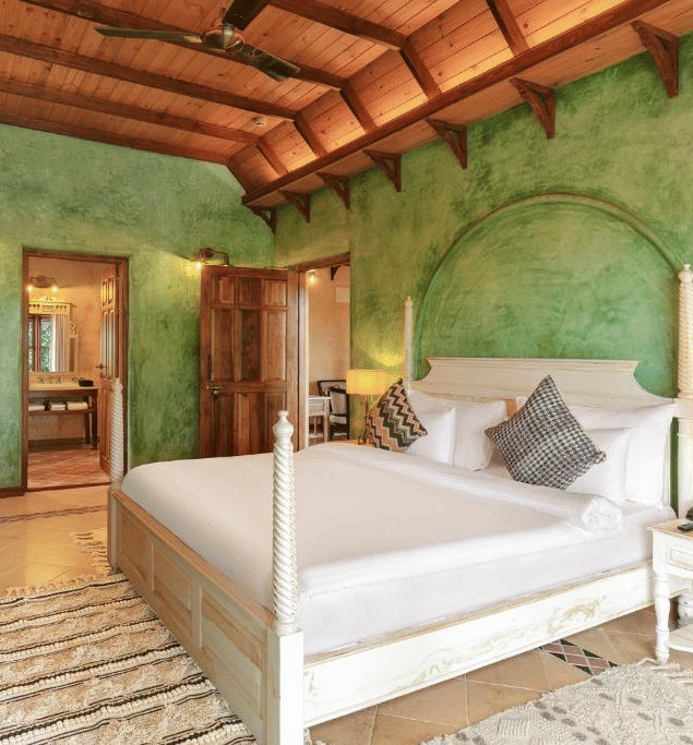 Guest room at Golden Tulip Goa, Mandrem Beach with a 4-poster king bed, green lime-washed walls, a flat-screen TV, and an en-suite bathroom view.
