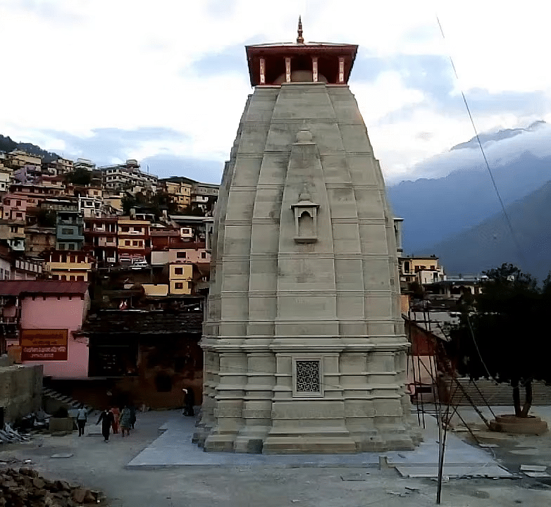 A stone temple with a pagoda-like roof stands in a town nestled in a mountainous landscape.