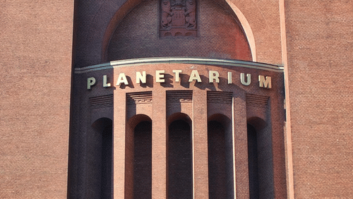 A facade view of a Planetarium Building made of red bricks with the blue sky in the background.