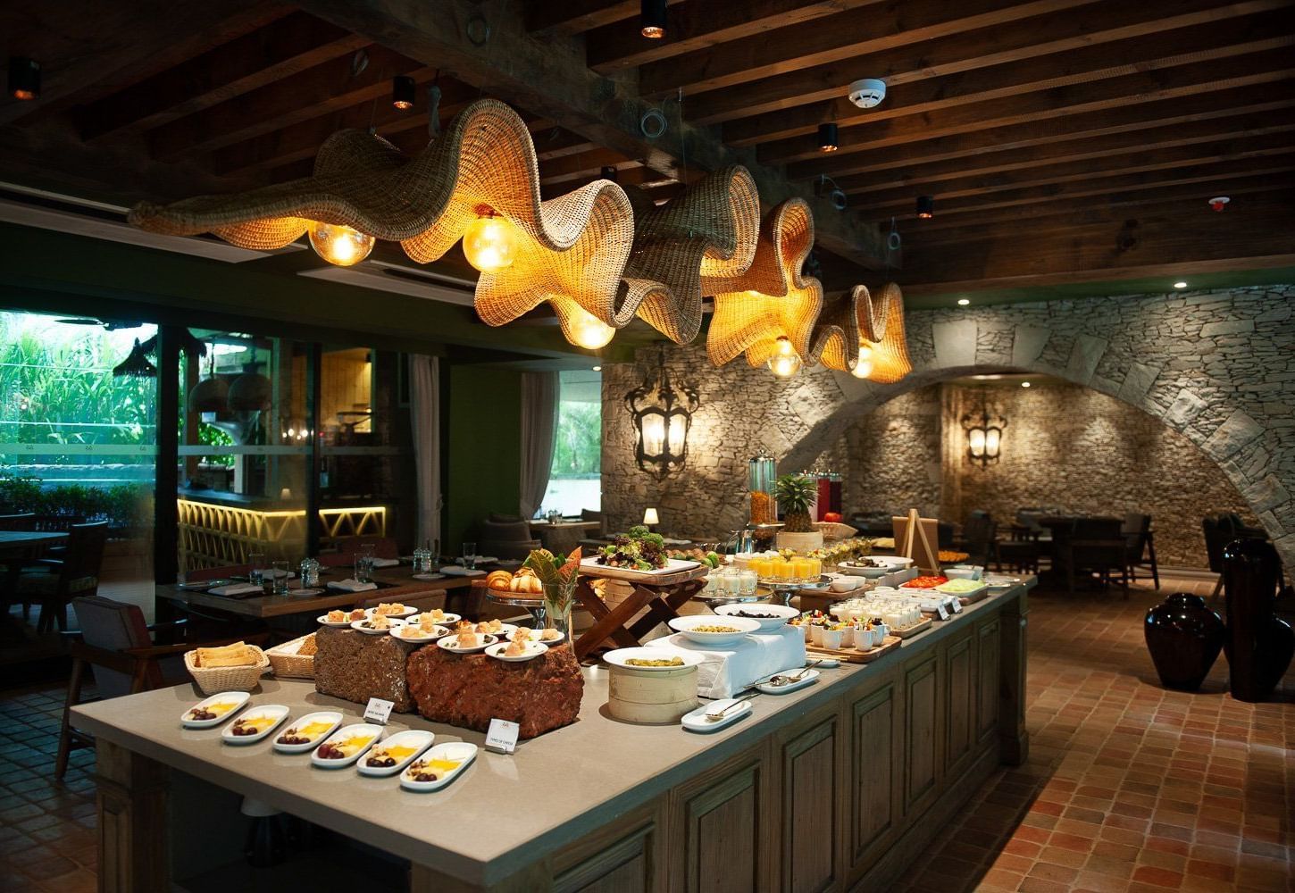 A lavish breakfast buffet spread at the Mila Restaurant at The Evren, Vagator, featuring a variety of dishes on display under the woven light fixtures.