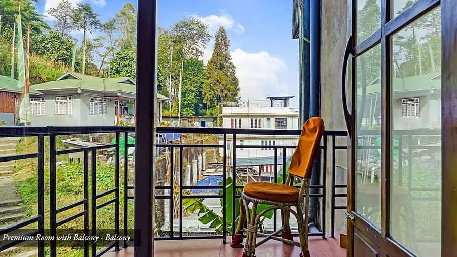 A side view of a chair placed on a balcony that has a view of greenery A front view of the beds placed in a room that has a glass window | Summit Newa Regency & Spa, Pelling