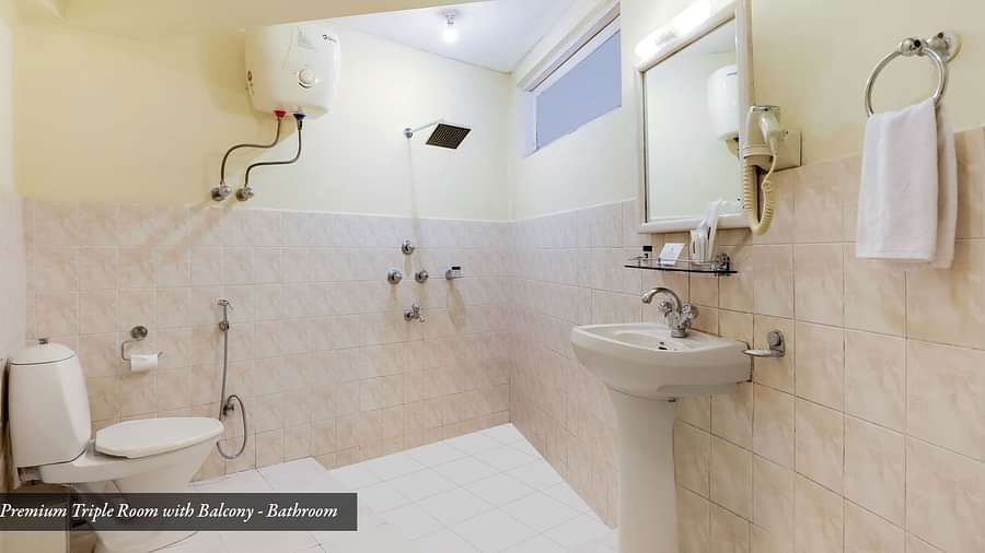 A commode, wash basin, and a mirror on the wall in the bathroom A front view of the beds placed in a room that has a glass window | Summit Newa Regency & Spa, Pelling