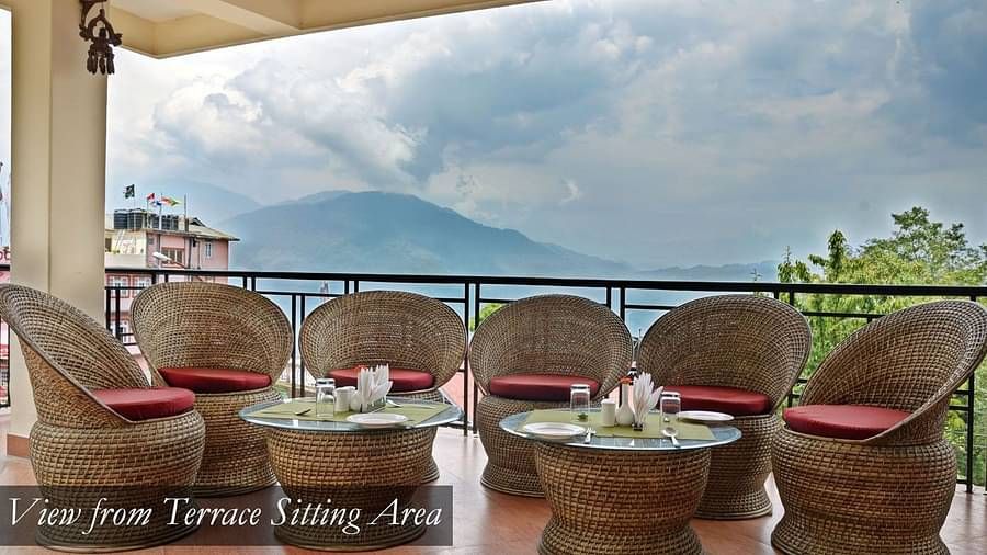Chairs and tables that are placed in the balcony with a backdrop of clear sky | Summit Newa Regency & Spa, Pelling
