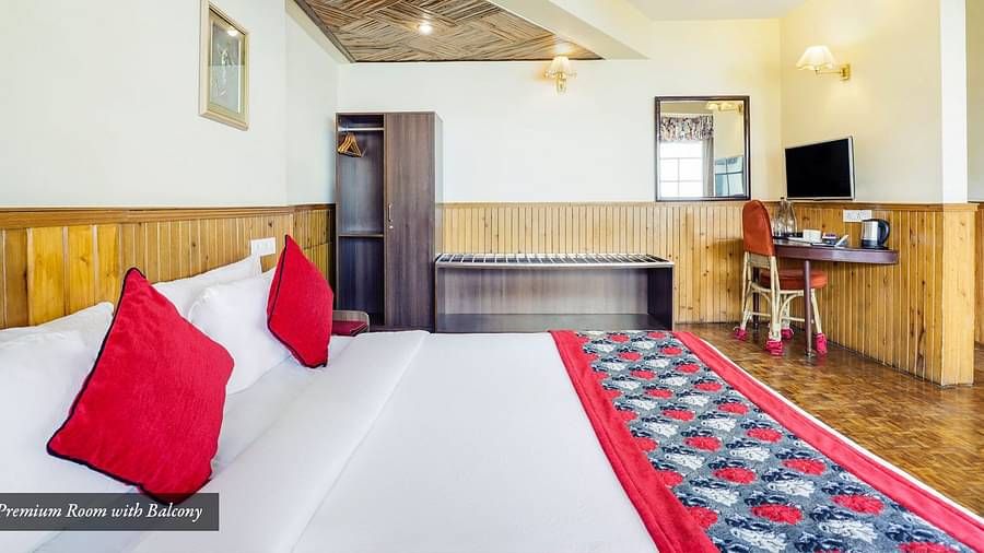 A side view of a bed in the room that has a TV, work desk, and a chair | Summit Newa Regency & Spa, Pelling