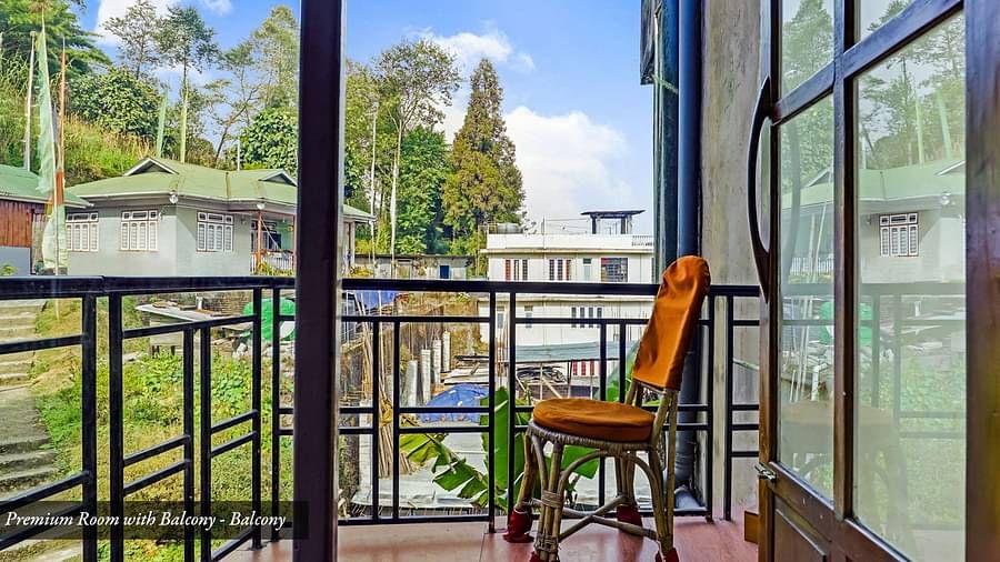 A side view of a chair placed on a balcony that has a view of greenery A front view of the beds placed in a room that has a glass window | Summit Newa Regency & Spa, Pelling