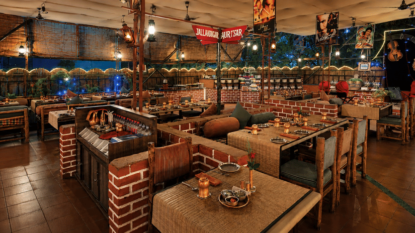 Open air restaurant at Pride Premier Pune with wooden tables, brick accents and evening lighting.