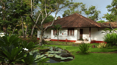 A traditional white cottage with a terracotta tile roof, red window frames, and a small porch, set in a lush tropical garden at Abad Turtle Beach Resort, Marari, Allappey, the best resort in Allappey