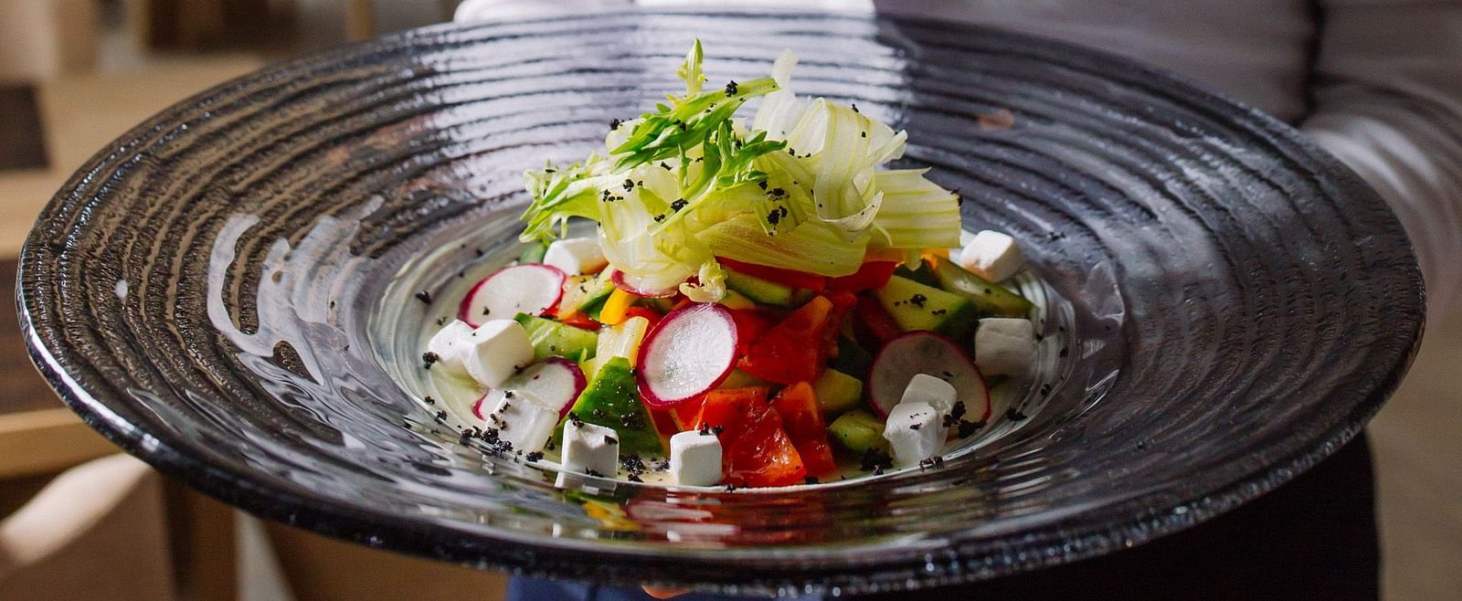 A waiter holding a beautifully plated dish wih fresh salad in a restaurant -  Sitara Luxury Hotel in Hyderabad near Ramoji Film City.