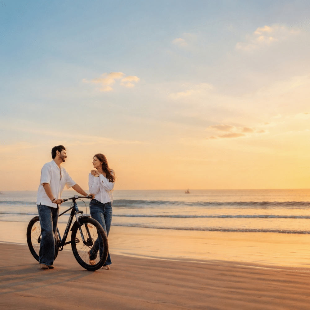 Two people with a bicycle on the sand at sunset, with fishing boats on the sea behind them, at MAYFAIR Palm Beach Resort, Gopalpur-on-Sea.