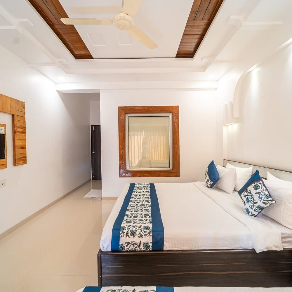 Deluxe Valley View Room featuring a bed with white and blue linens, a dark wood headboard, a side table, and a wall-mounted television, with neutral-toned walls and ceiling
