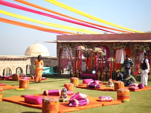 A vibrant outdoor event is set up on a green lawn at Tijara Fort-Palace - 19th Century, Alwar with clear blue sky in the background.