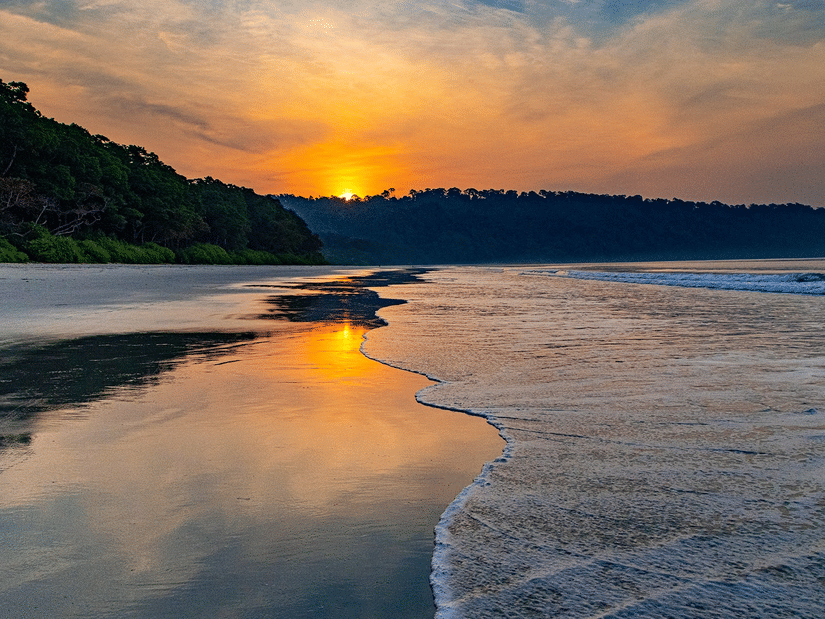 Radhanagar Beach during a sunset with the reflection of the sun on the water with shallow waves crashing the shore
