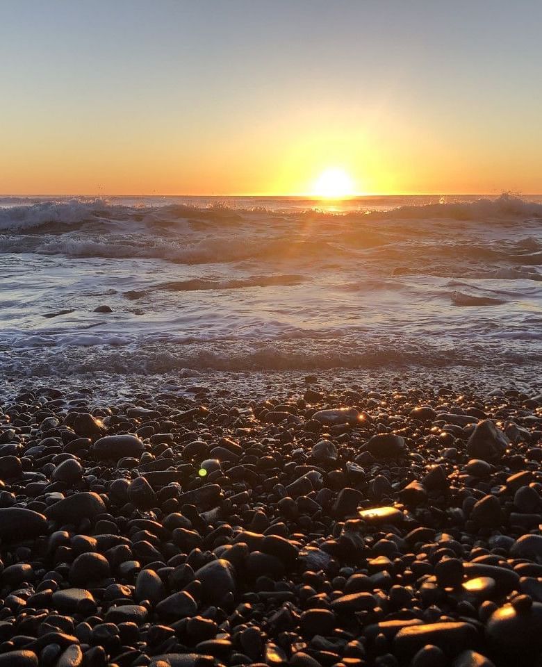 Sunset over an ocean seen from a shower covered in pebble rocks - Brewery Gulch Inn & Spa