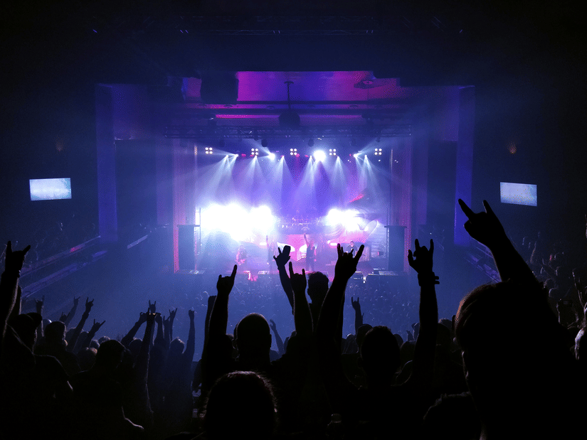 Music fans raising their hands and cheering during an energetic indoor concert with dramatic lighting effects